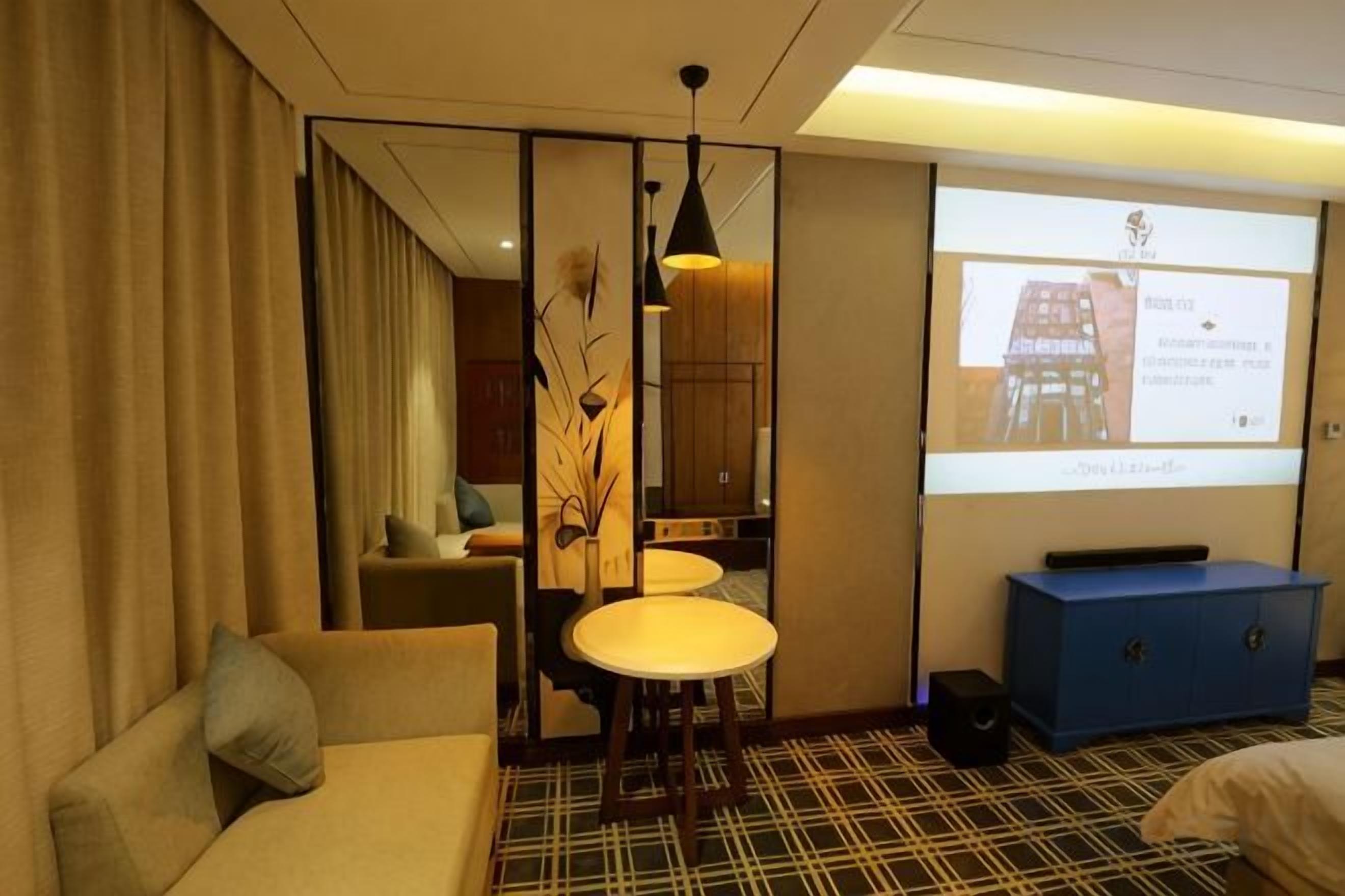 Habitación de hotel con sofá, una pequeña mesa de comedor, una pantalla para proyector y un armario azul.