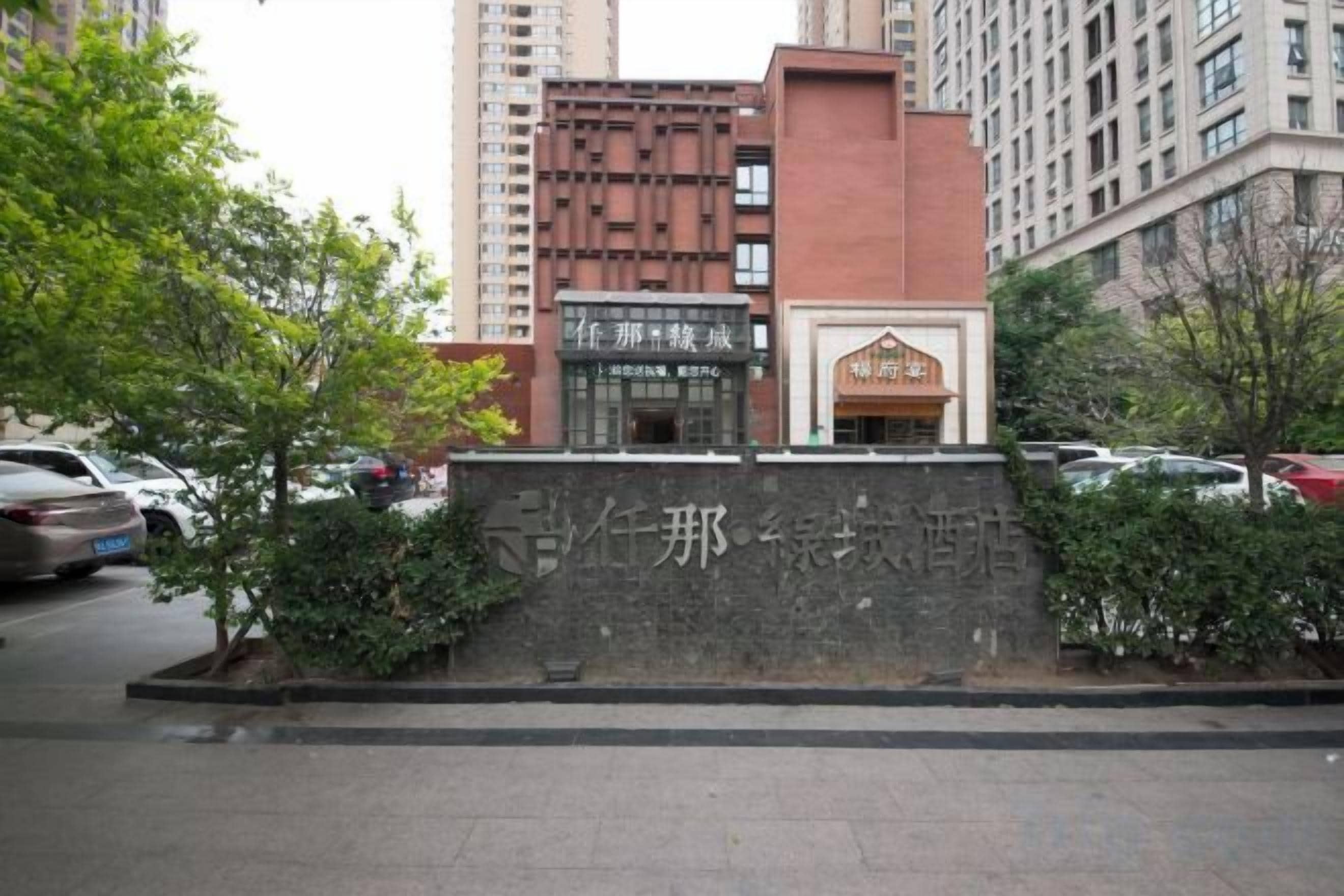 A building with a stone wall and a sign with Chinese characters, surrounded by trees and parked cars.