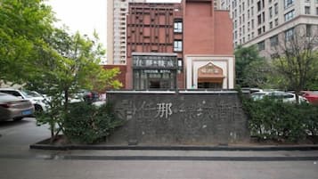 A building with a stone wall and a sign with Chinese characters, surrounded by trees and parked cars.