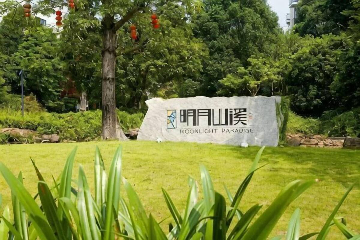 A sign with text and a logo, surrounded by greenery and trees.