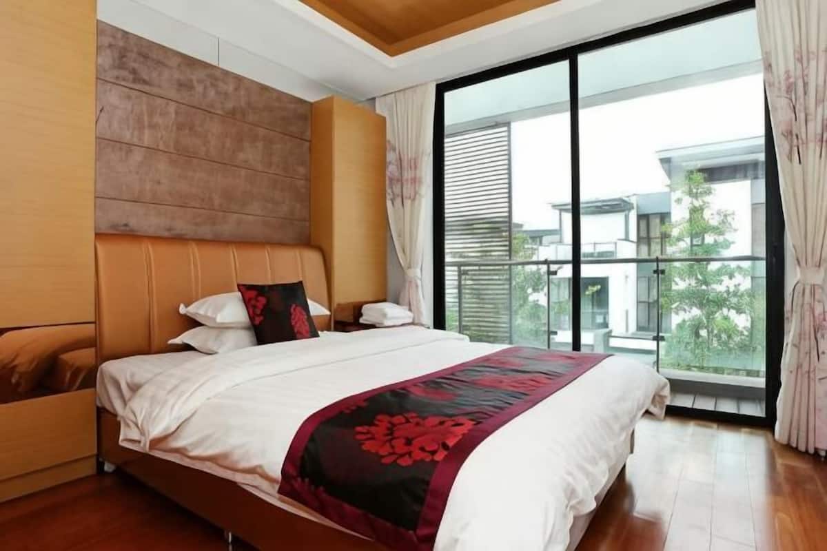 A modern hotel room with a large bed, a wooden headboard, a balcony with a view, and a large window.