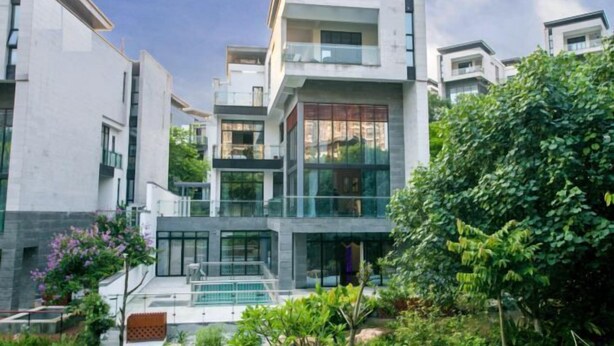 Un moderno edificio residenziale a più piani con facciata in vetro, terrazza sul tetto e area giardino curata.