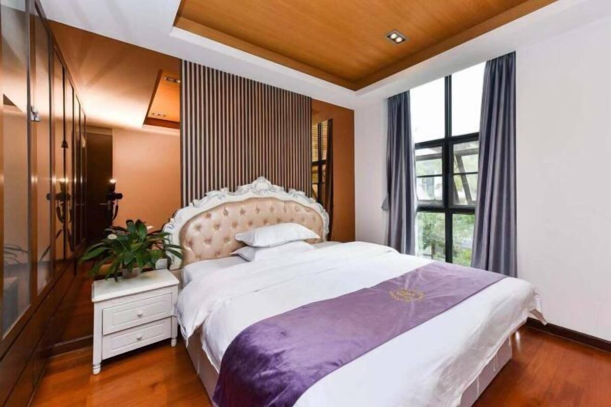 A bedroom with a bed, nightstand, and potted plant.