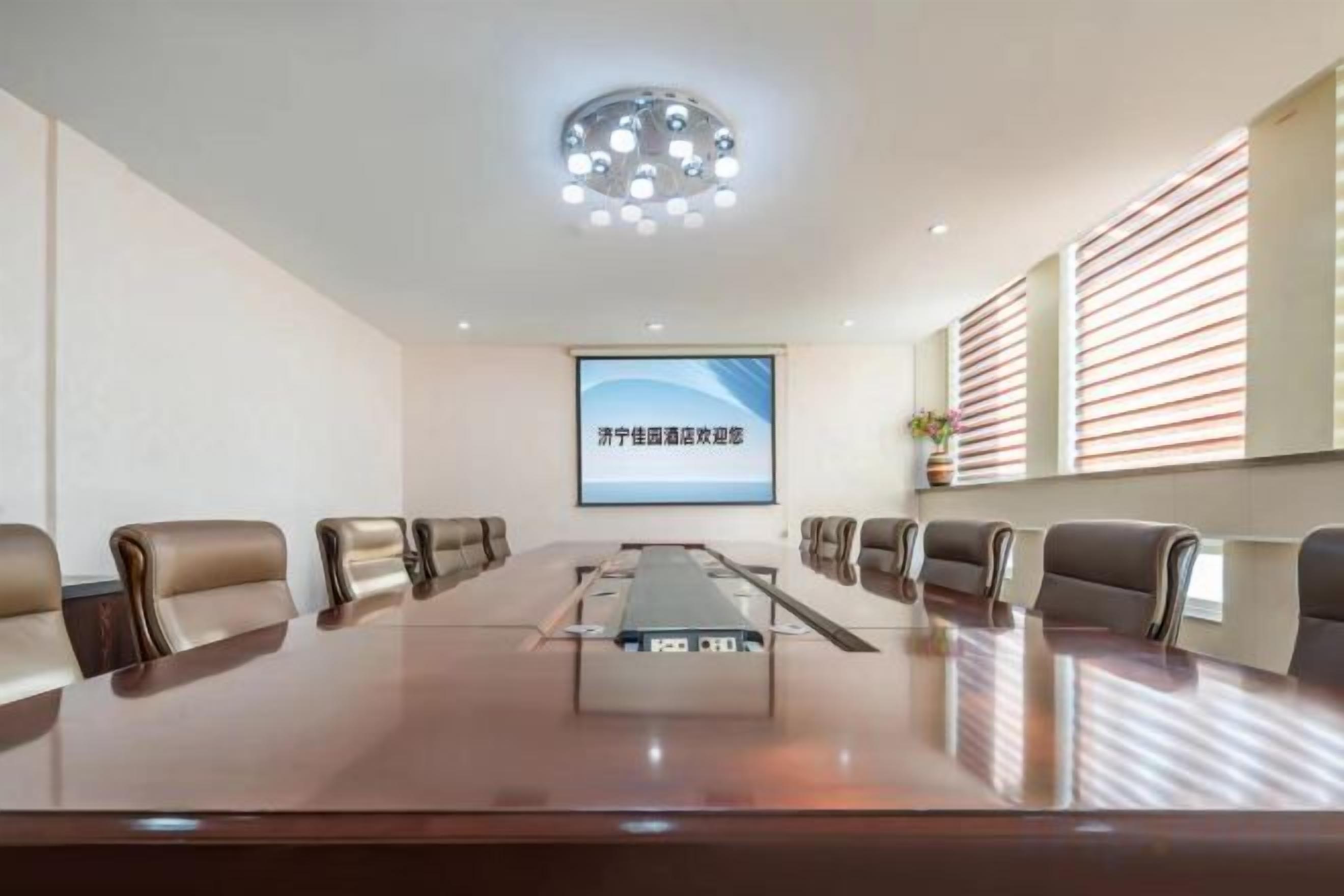Una sala de conferencias con una larga mesa, sillas, una pantalla de proyector y una lámpara en el techo.