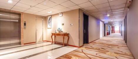 A hotel corridor with a marble floor, elevator, and a reception desk.
