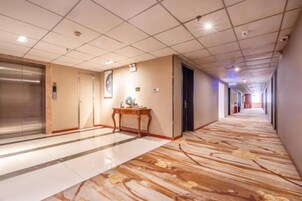 A hotel corridor with a marble floor, elevator, and a reception desk.