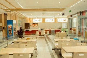 A modern restaurant interior with multiple dining tables and chairs, a kitchen area, and a counter. - Jia Yuan Hotel (Jining)