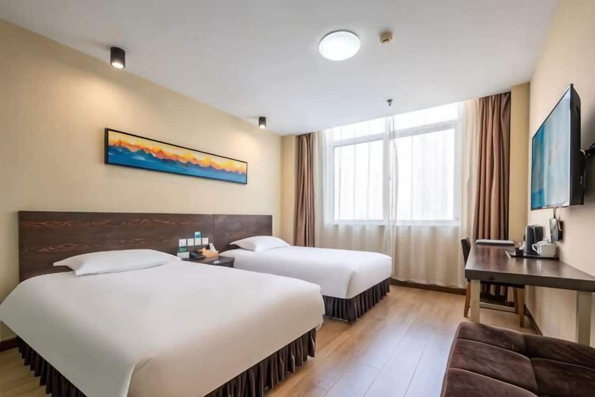 Habitación de hotel con dos camas, un escritorio, un televisor y un cuadro en la pared.