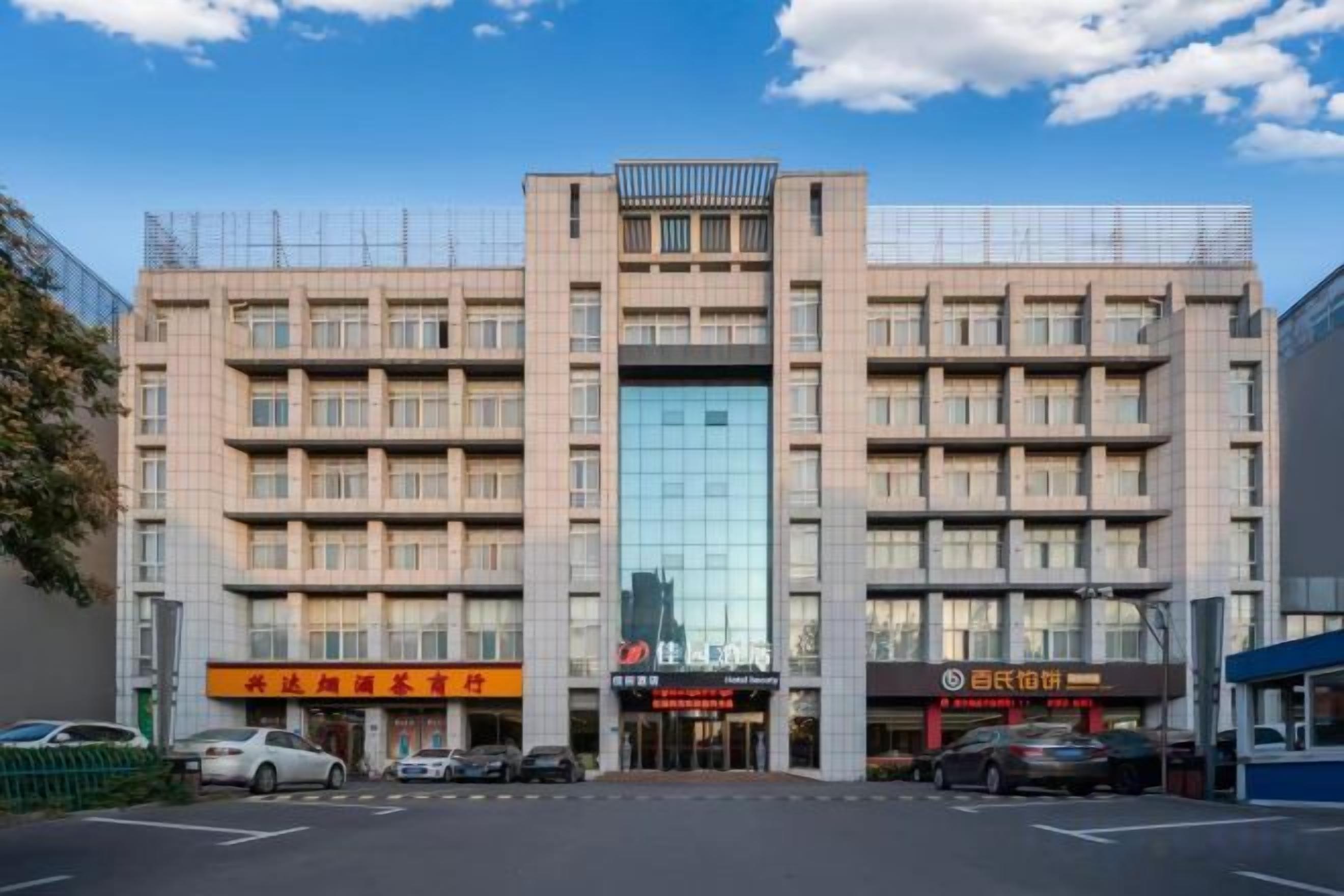 A multi-story building with a central glass facade, multiple ground-level commercial spaces, and a parking lot.
