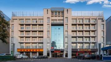 A multi-story building with a central glass facade, multiple ground-level commercial spaces, and a parking lot.