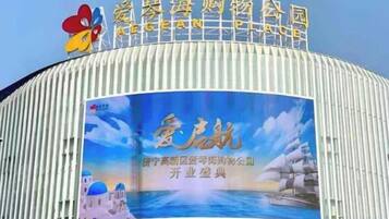 Un edificio curvo con un letrero que dice '爱罗海购物公园' y un cartel grande con texto y un fondo de cielo azul.