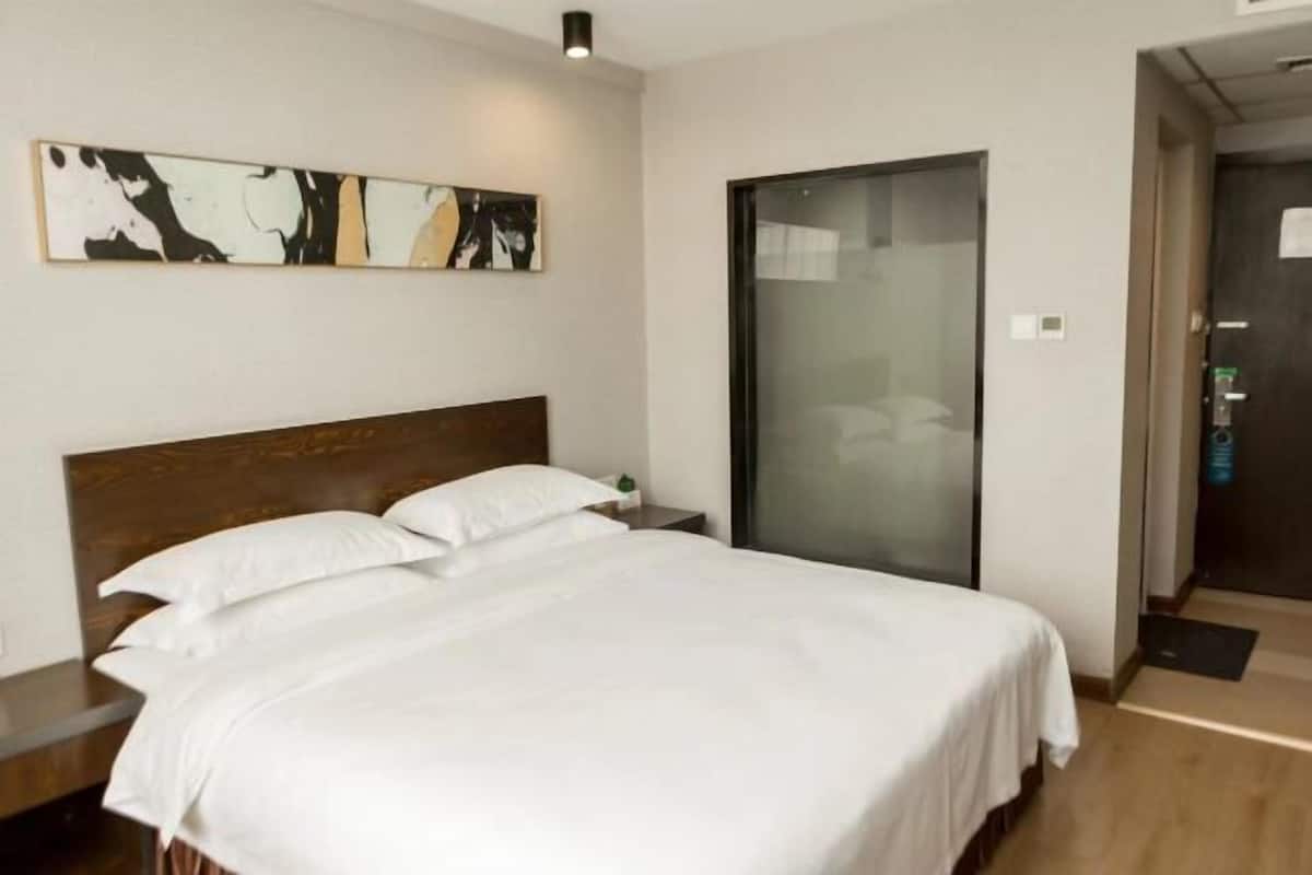 Una habitación de hotel con una cama grande, cabecera de madera, mesita de noche, una obra de arte abstracta en la pared y una puerta corredera.