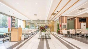A modern hotel lobby with a central reception desk, seating areas, and a large plant.