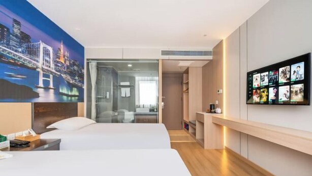 A hotel room with a bed, a desk, a TV, and a cityscape painting.