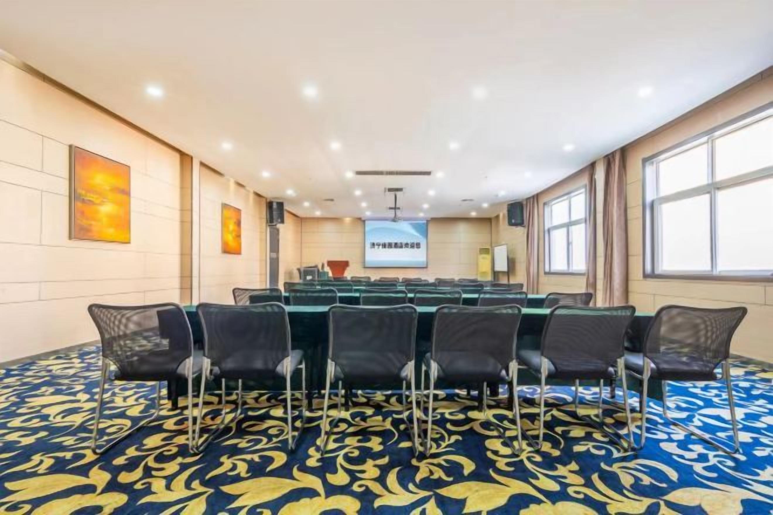A conference room with a long table, chairs, a projector screen, and a carpeted floor.