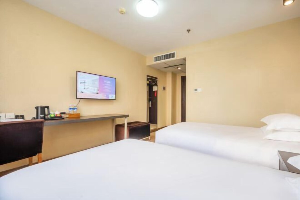 A hotel room with two beds, a desk with a computer, and a TV mounted on the wall.