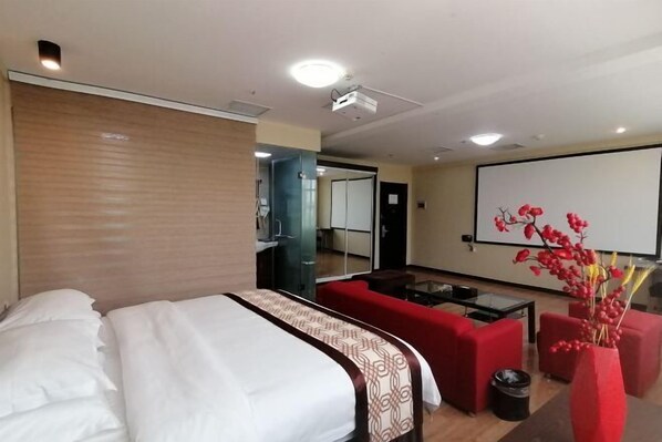 A hotel room with a bed, a red sofa, a small table, and a projector screen. - Jia Yuan Hotel (Jining)