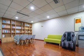 A room with a wooden floor, a green sofa, a massage chair, and a bookshelf filled with books. - Jia Yuan Hotel (Jining)