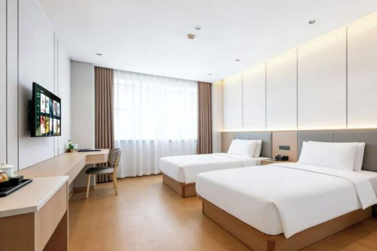 Habitación de hotel con dos camas, un escritorio, una silla, un televisor y una ventana con cortinas.