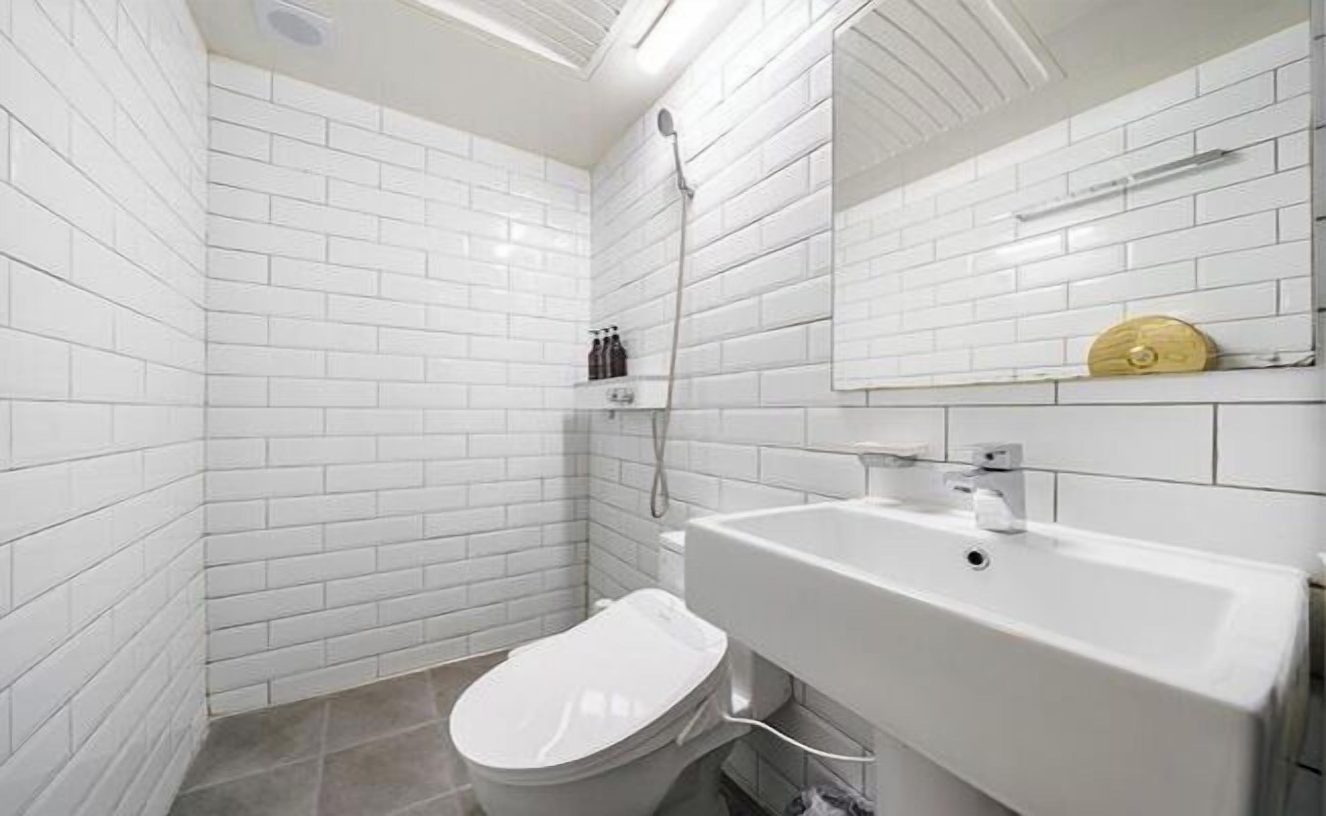 A bathroom with white subway tiles, a white toilet, a white sink, and a shower.