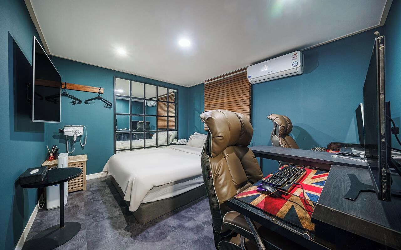 A hotel room with a bed, a desk with a computer, a chair, a mirror, and a window with blinds.