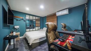 A hotel room with a bed, a desk with a computer, a chair, a mirror, and a window with blinds.