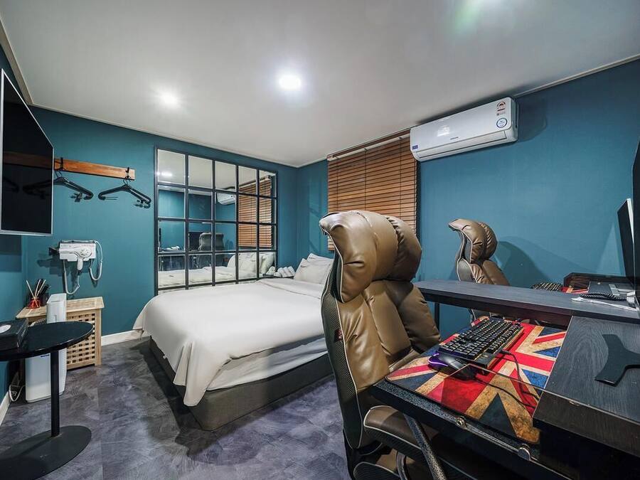 A hotel room with a bed, a desk with a computer, a chair, a mirror, and a window with blinds.
