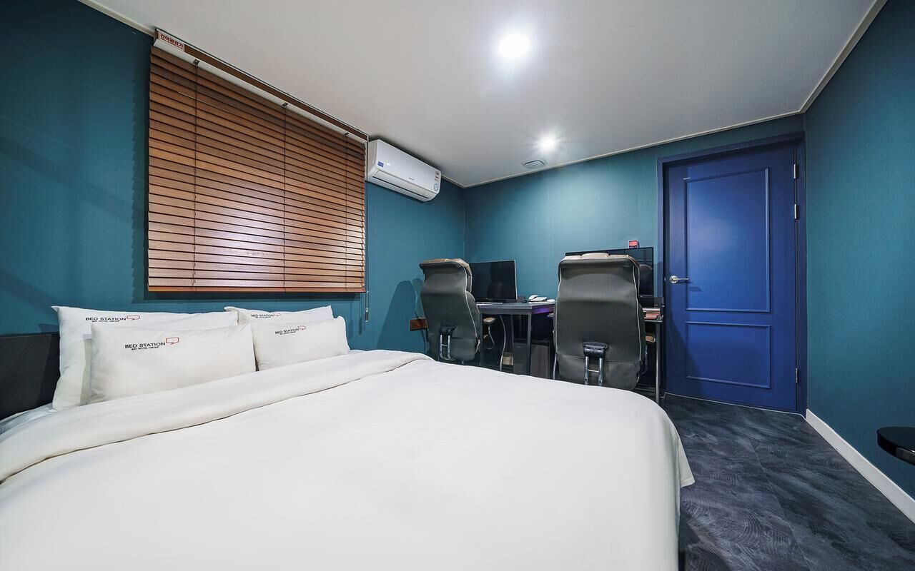 Une chambre d’hôtel avec un lit, deux chaises, un bureau, un ordinateur et une porte bleue.