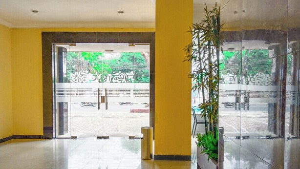A spacious lobby with a polished floor, a large glass door leading outside, and a potted plant on the right. - Hotel Labuhan Raya (Medan)