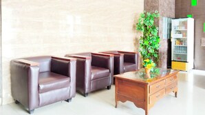 A lobby with leather chairs, a wooden coffee table, and a refrigerator with a green sign. - Hotel Labuhan Raya (Medan)