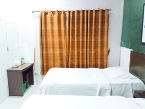 A hotel room with a bed, a small bedside table, a green trash bin, and a curtain. - Hotel Labuhan Raya (Medan)