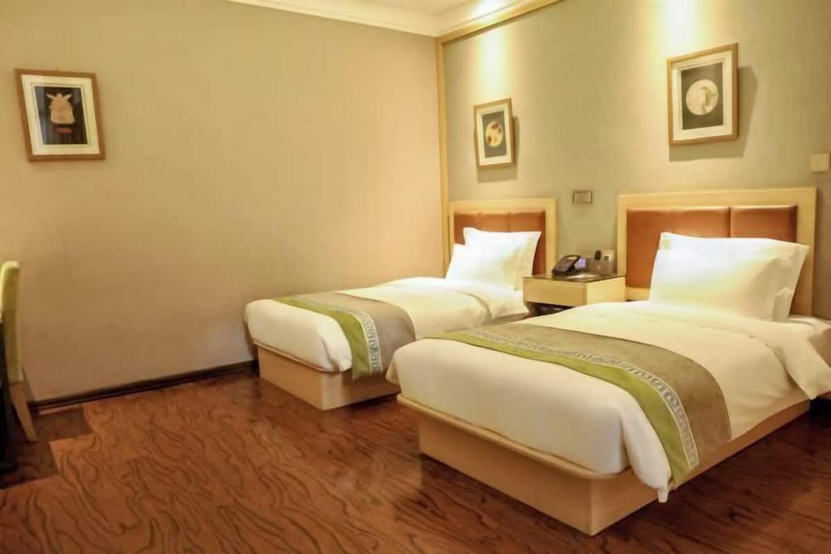 Une chambre d’hôtel avec deux lits, un plancher en bois et des tableaux encadrés aux murs.