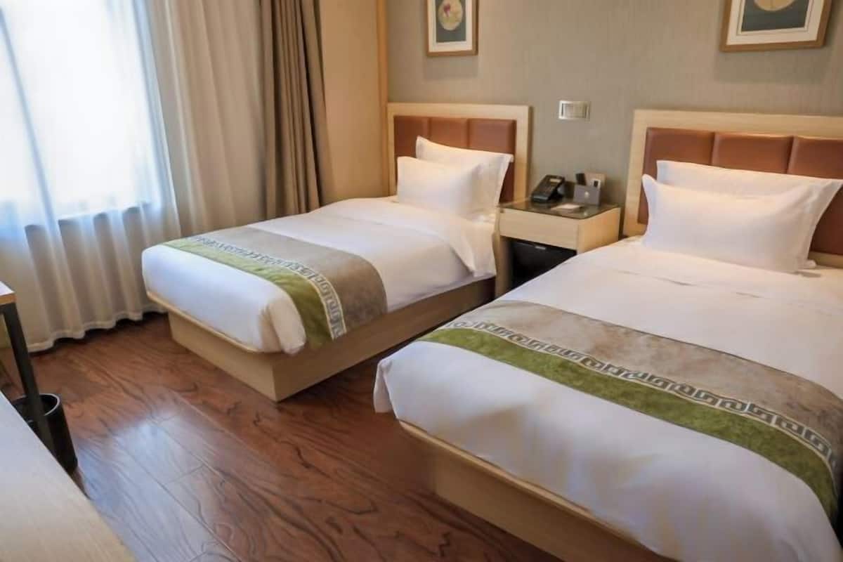 Une chambre d’hôtel avec deux lits, une table de chevet avec un téléphone et une fenêtre avec des rideaux.