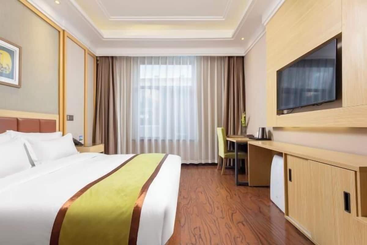 Une chambre d’hôtel avec un lit, un bureau, une télévision et une fenêtre avec des rideaux.