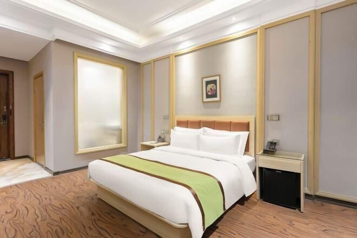 Une chambre d’hôtel avec un grand lit, une table de chevet, une commode et un tableau accroché au mur.