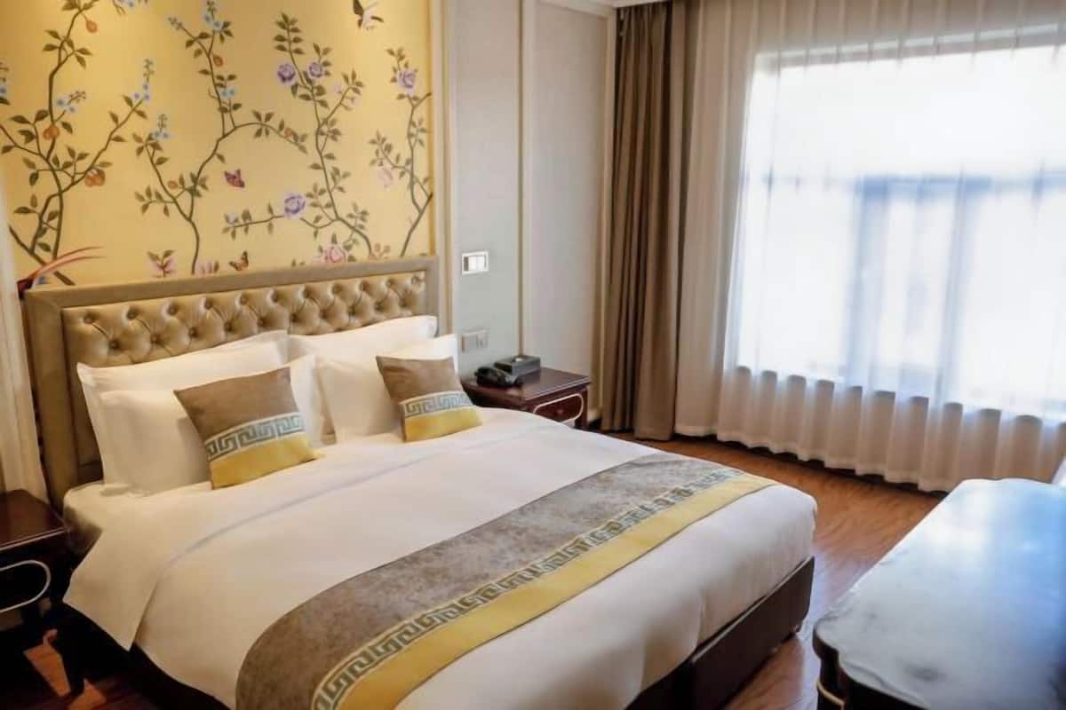 Une chambre d’hôtel avec un grand lit, une table de chevet, une table et une fenêtre avec des rideaux.