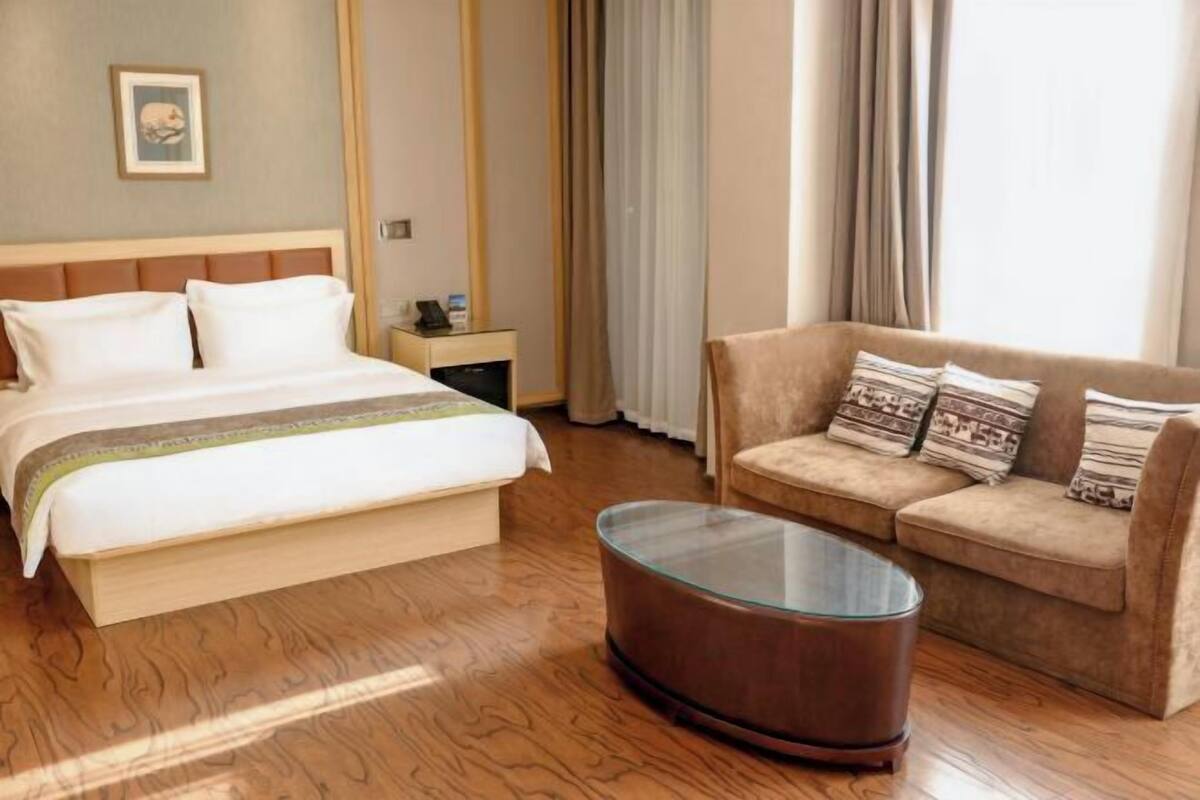 Une chambre d’hôtel avec un lit, un canapé, une table basse en verre et une table de chevet.