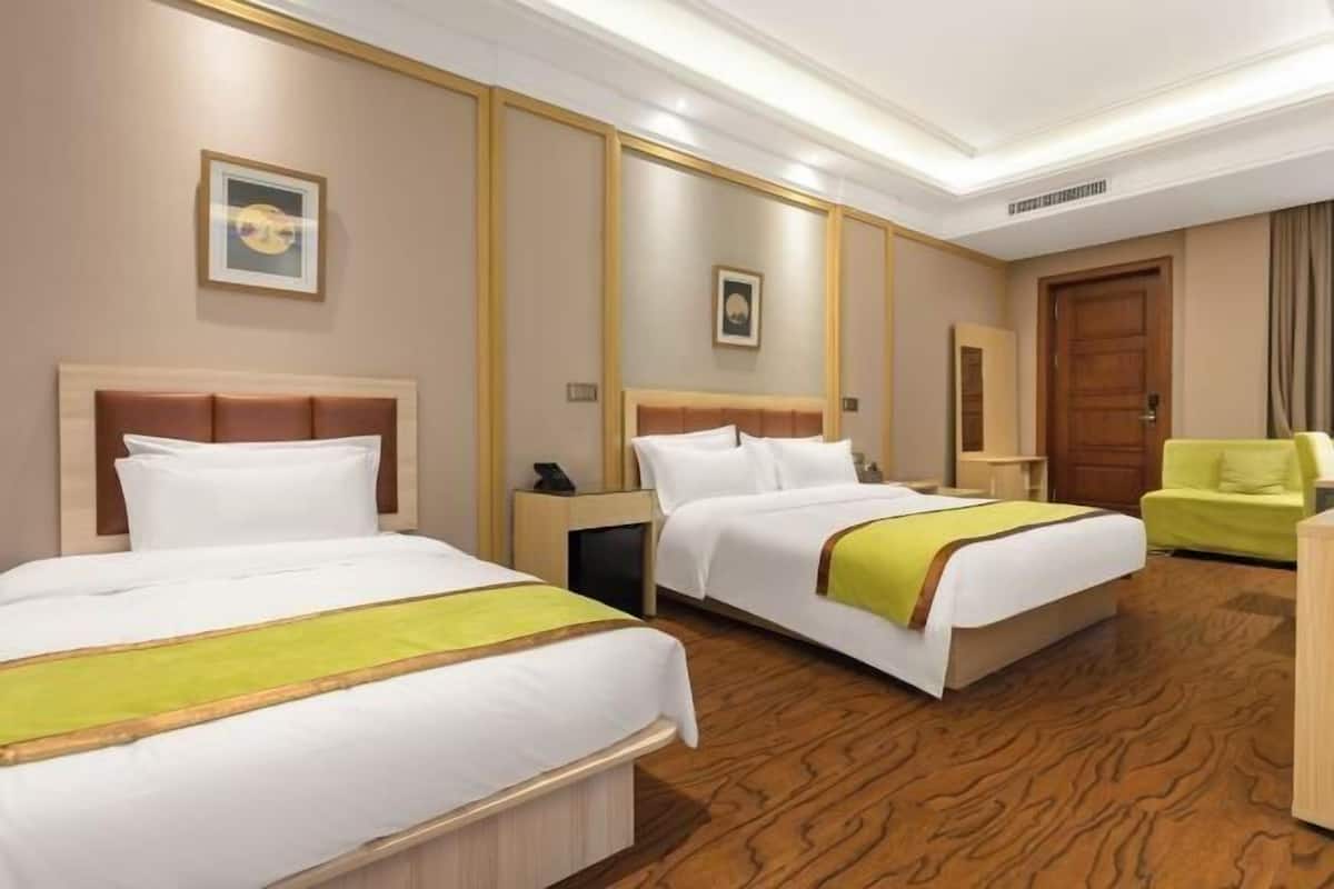 Une chambre d’hôtel avec deux lits, un plancher en bois, une chaise verte et une porte en bois.
