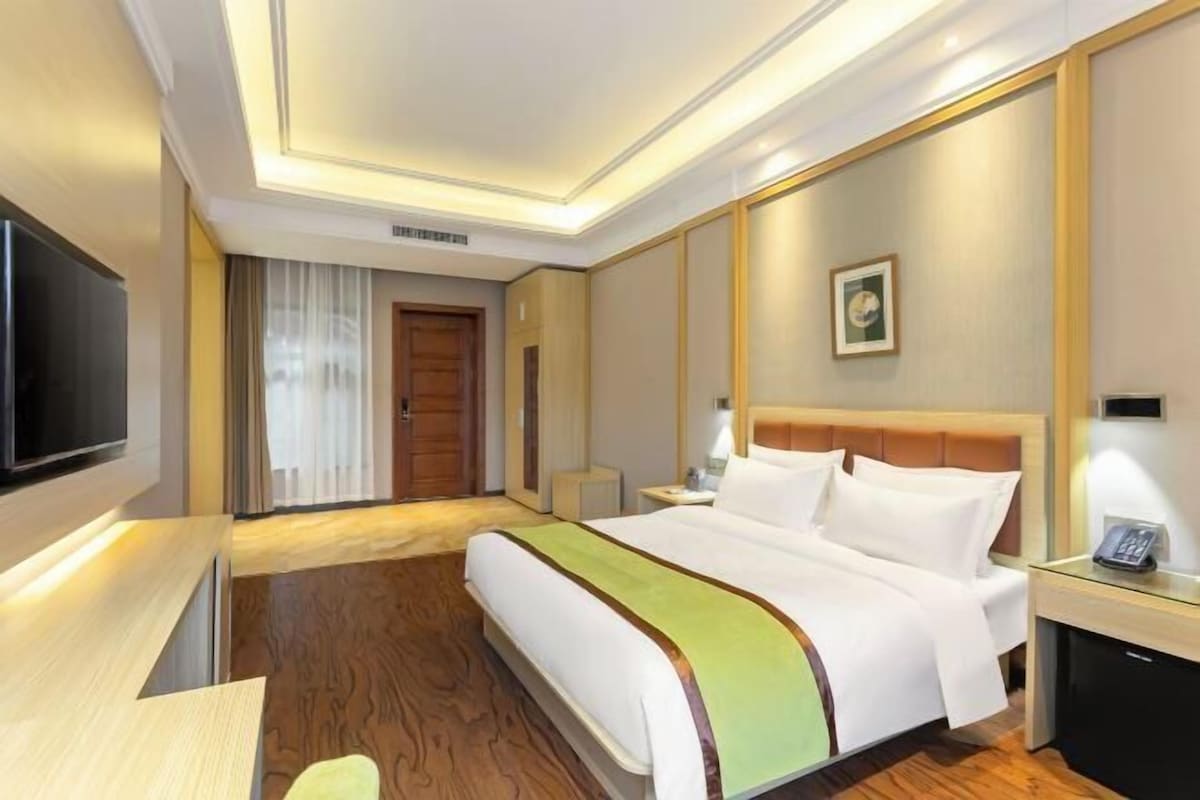 A hotel room with a large bed, a flat-screen TV, a bedside table, and a wooden floor.