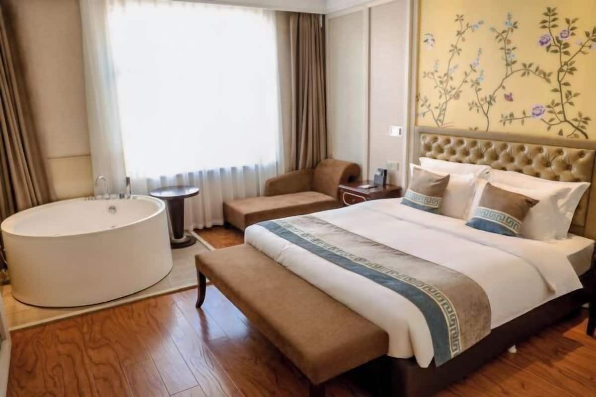 Une chambre d’hôtel avec un grand lit, un canapé séparé, une baignoire ronde et une fenêtre avec des rideaux.