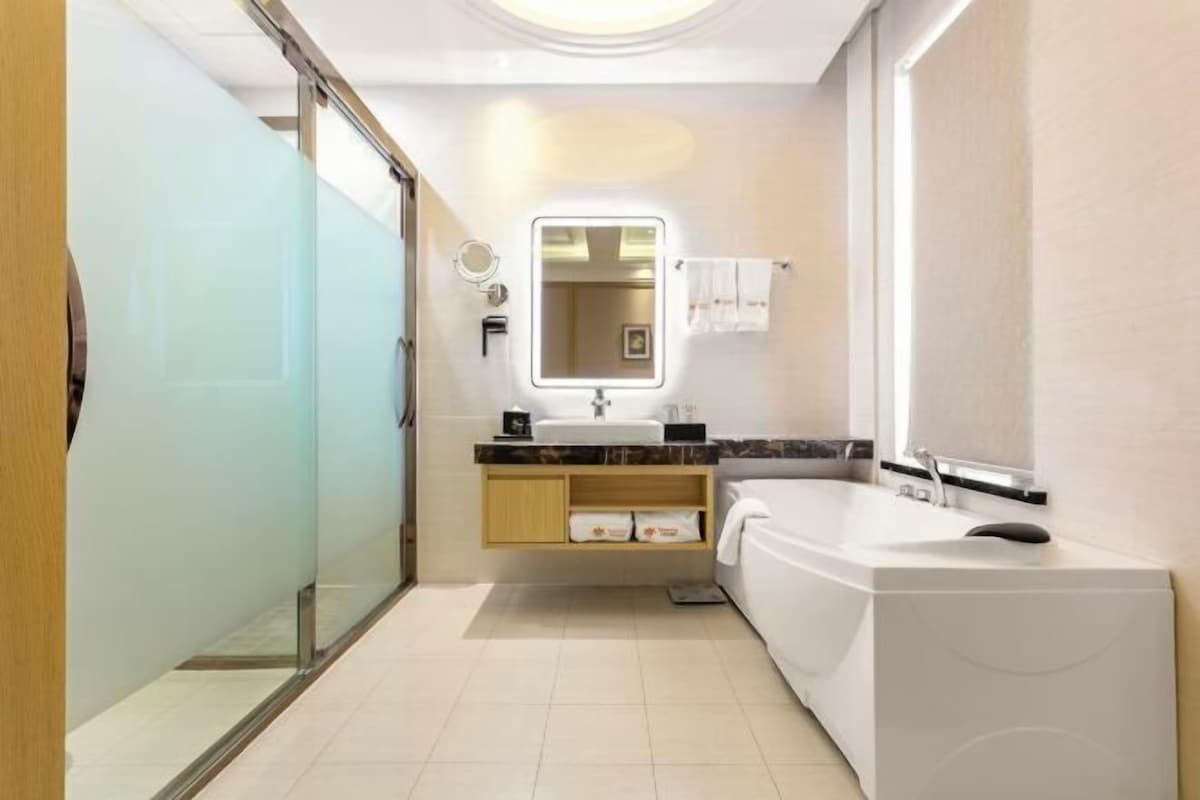 A modern bathroom with a glass shower enclosure, a large bathtub, a vanity with a mirror, and a towel rack.