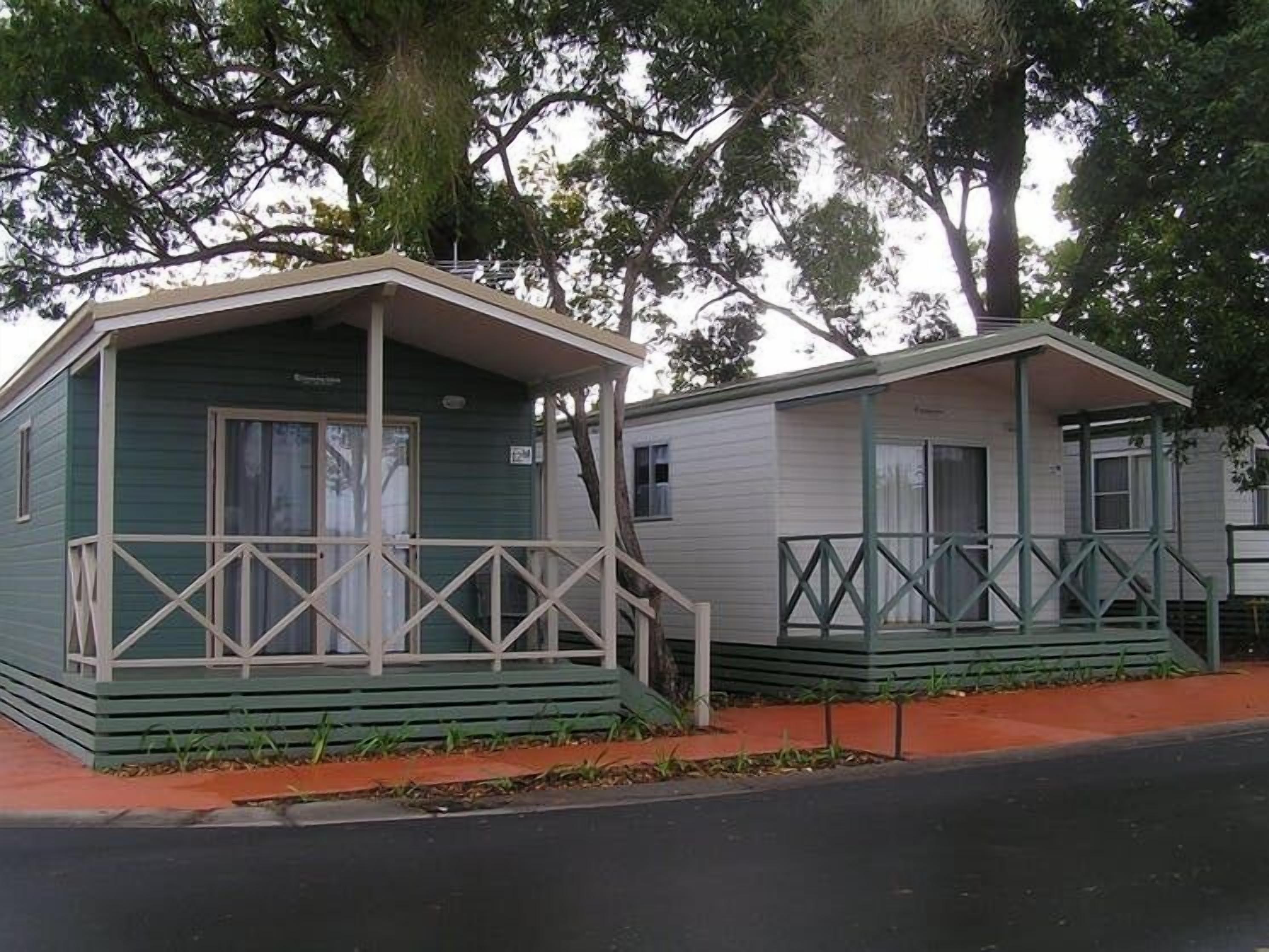 Two small, single-story cabins with green siding and white trim, each featuring a porch with a railing.