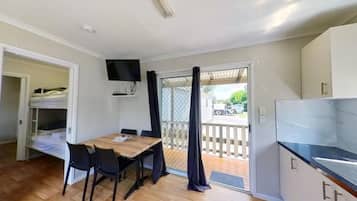 Una habitación compacta con una mesa de comedor de madera, sillas negras, un televisor montado en la pared y un ventanal corredero que da a una terraza al aire libre.