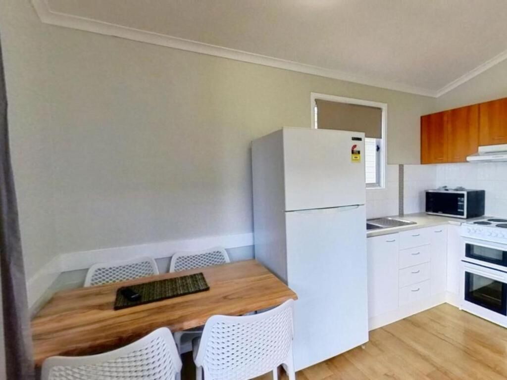 A compact kitchen with a refrigerator, microwave, stove, and white cabinetry.