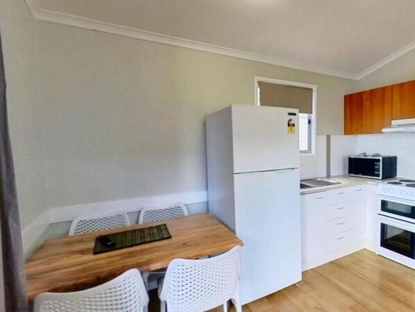 Una cocina compacta con refrigerador, microondas, estufa y alacenas blancas.