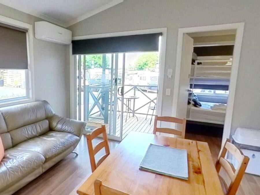 Un salon avec une table en bois, un canapé en cuir et une porte-fenêtre coulissante donnant sur un espace extérieur doté d’un balcon.