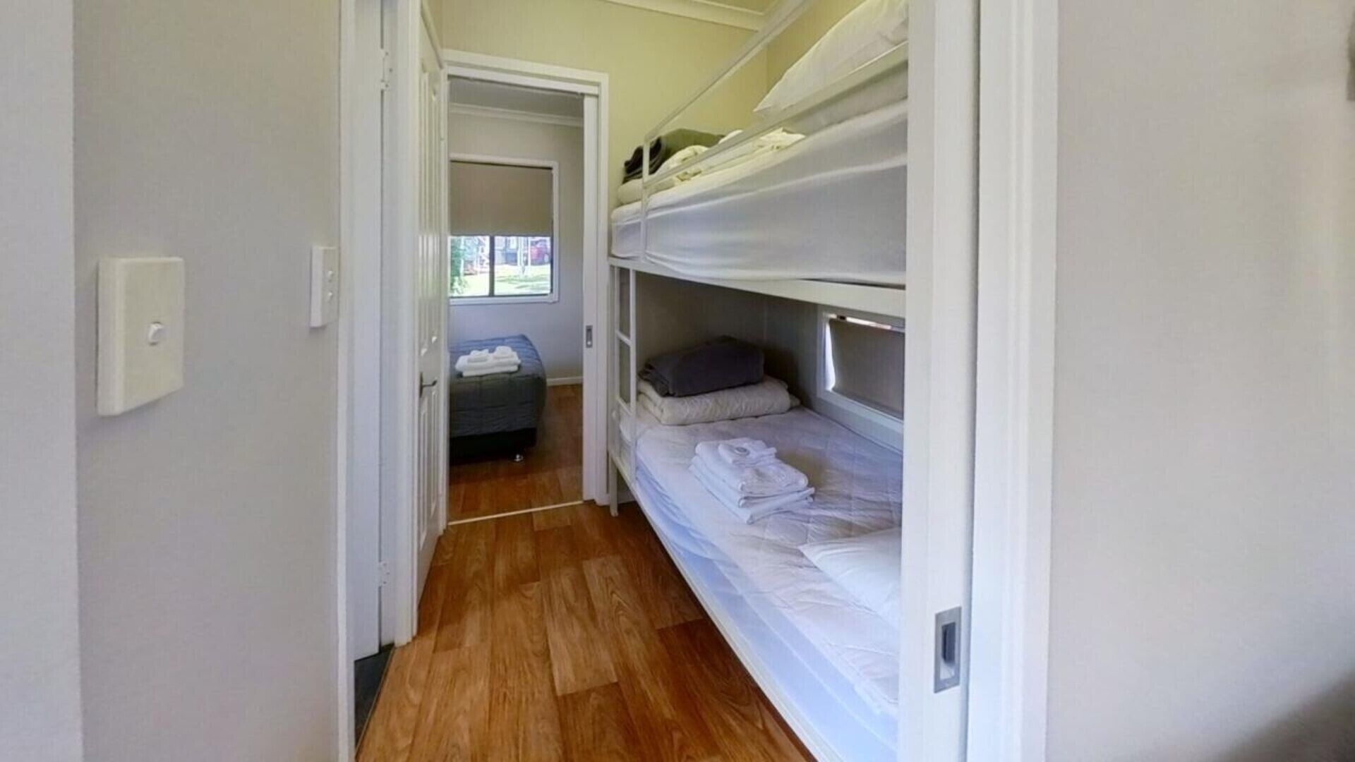 A narrow hallway leading to a bunk bed room with a small window.