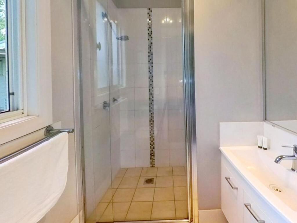 A modern bathroom with a glass-enclosed shower, a white sink, and a tiled floor.
