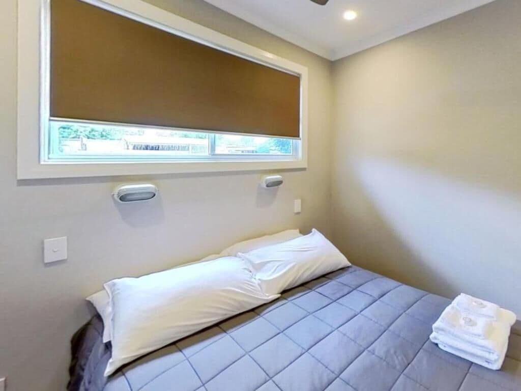 A bedroom with a bed, a window with blinds, and a towel on the floor.