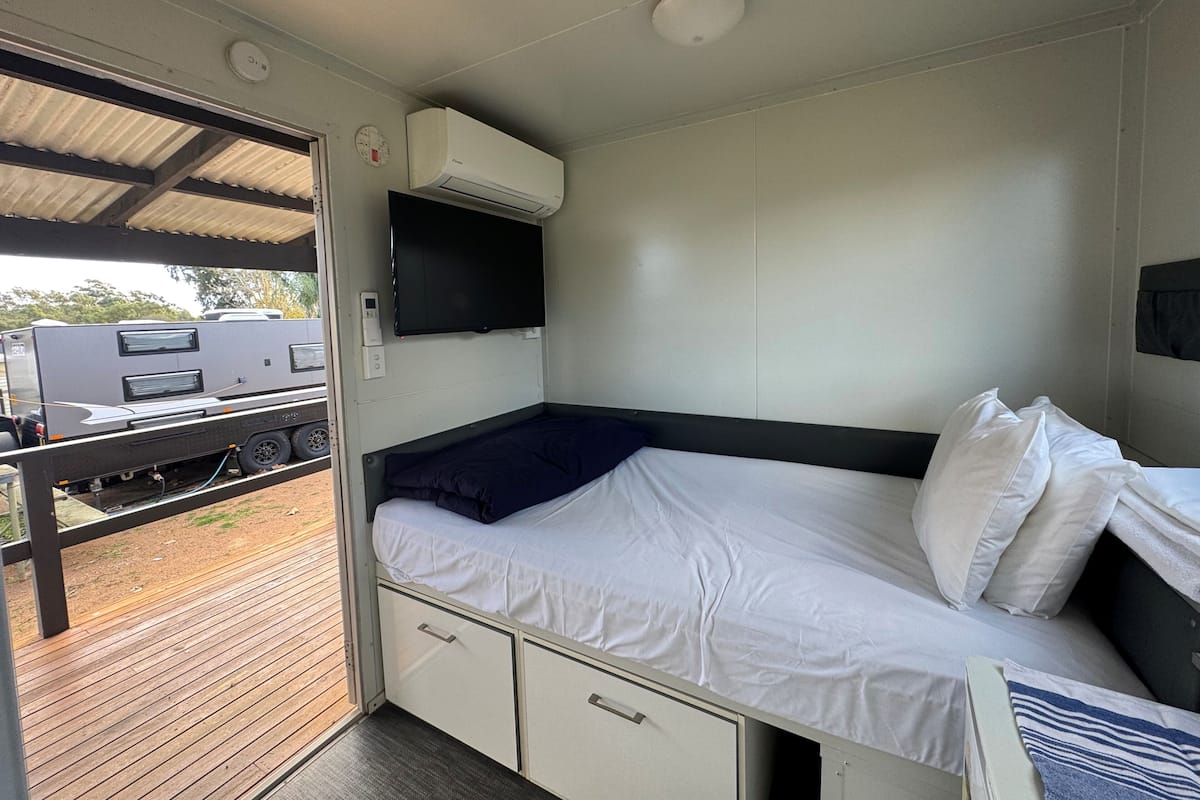 A compact RV bedroom with a bed, a mounted TV, and a small kitchenette area.